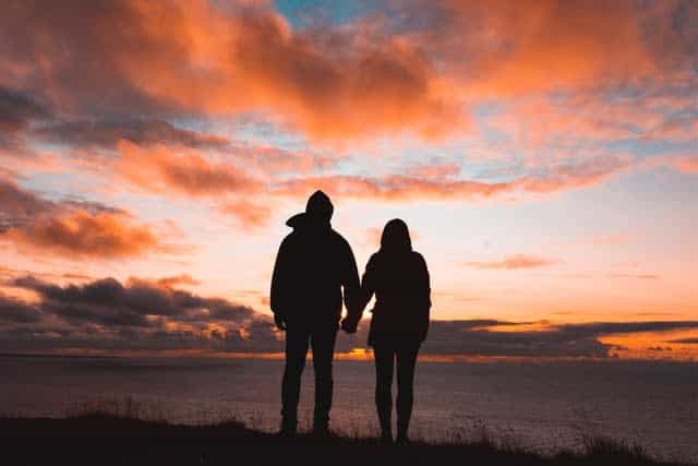 Man and woman holding hands in front of sunset