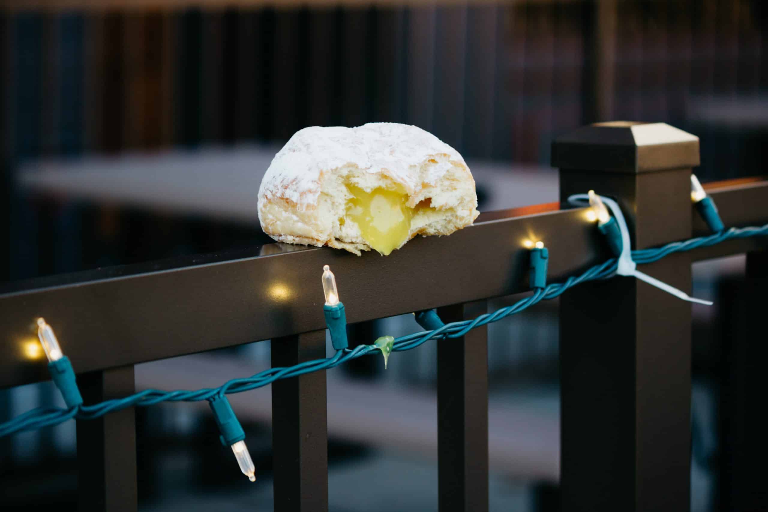 Donut with bite taken out of the, sitting on a railing, dripping filling onto xmas lights.