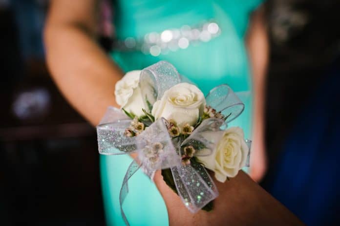 Close up of a white rose, silver bowed corsage on a person's arm