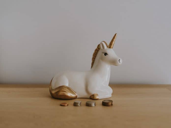 White and gold ceramic unicorn figurine set on a table, with four stacks of coins in front of it