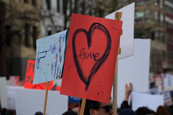 Protest signs being held up in a big group, one visible showing heart with word love in center