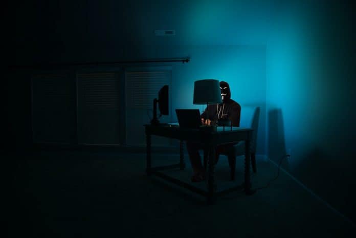 Person with mask on, sitting at a desk in an empty room, typing on a computer