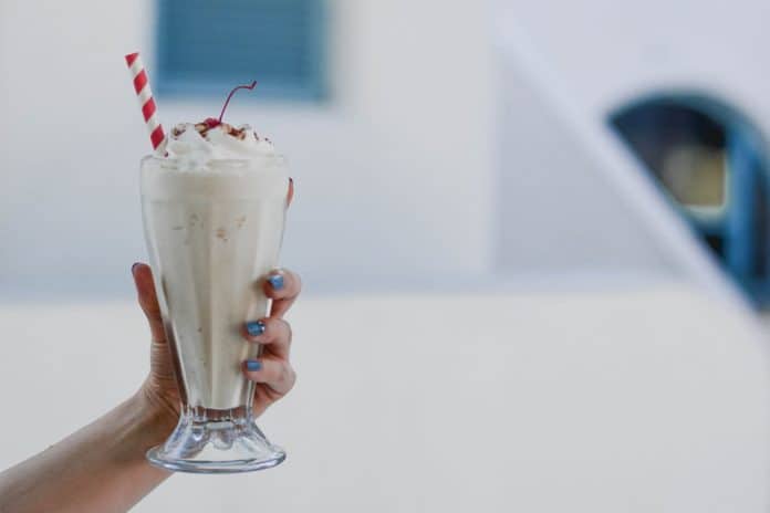 Hand holding a glass of a vanilla milkshake with a red and white striped straw