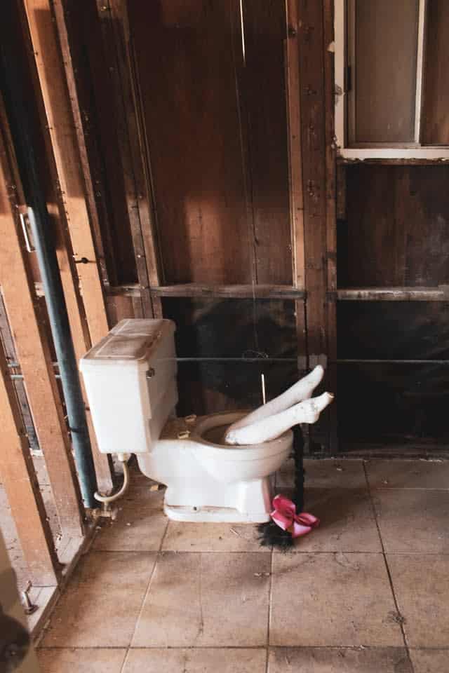 Toilet, not connected, in demo house, with mannequin legs sticking out of bowl