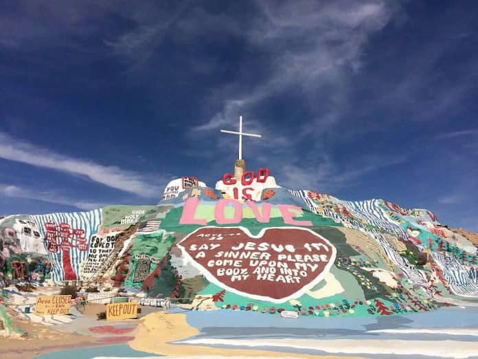 Colorful, multi-layered salvation mountain with cross at very top
