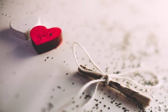 White and red wooden hearts next to each other, surrounded by confetti, and a small note tied with twine