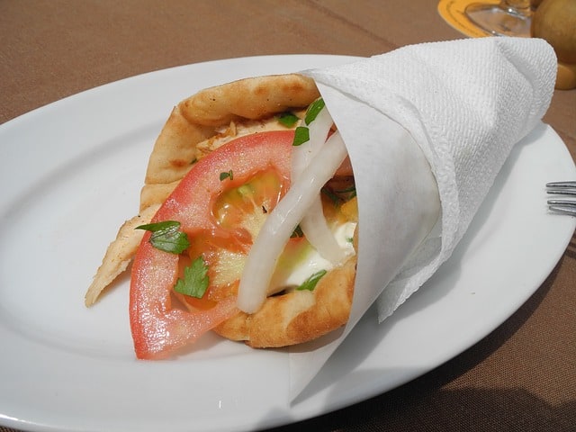 Gyro sandwich wrapped up with white paper, can see tomato, onion, and sauce at the top of the wrap