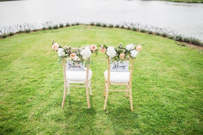 Two wedding chairs set next to each other side, on the back of one says 