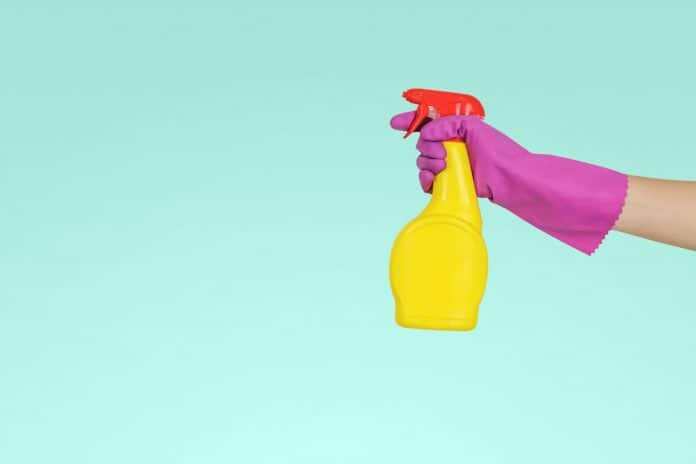 Teal background, with pink gloved hand holding a spray cleaning bottle in frame