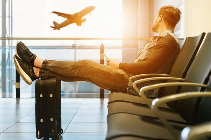 Man sitting with feet on suitcase, looking out airport window at plane