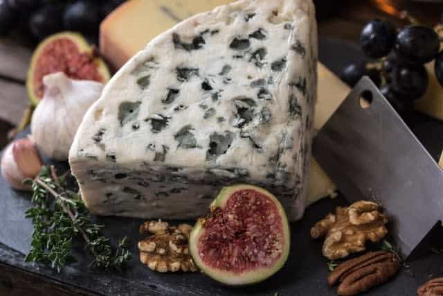 Wedge of soft blue cheese, surrounded by figs, nuts, and cheese knife