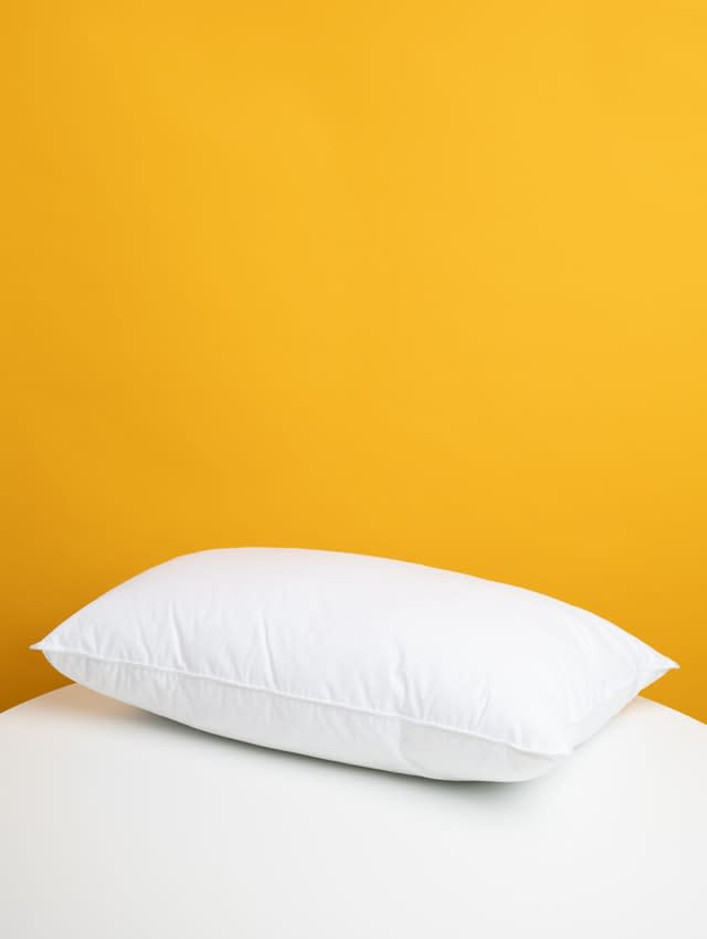 Yellow wall with white sheet and pillow in front