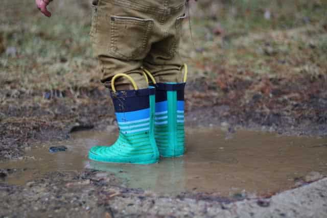 Kid wearing rain boots, standing in a muddy puddle