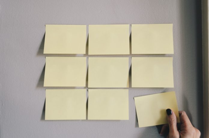 Grid of post-it notes on a wall, with a hand placing the final one finish the full grid