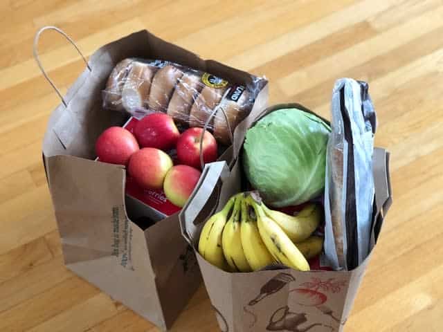 Two grocery bags filled with fruits, veggies, and breads