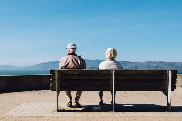 Older couple sitting on bench, looking out at mountain view