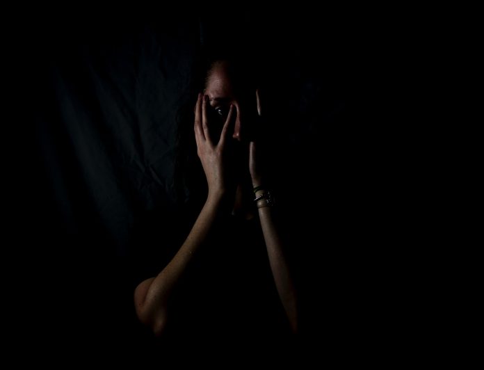 Woman in the shadows, covering her face with her hands