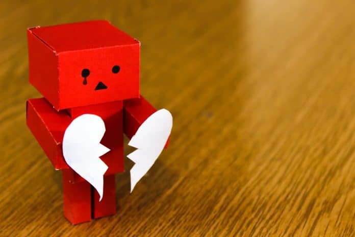 Small red toy robot holding a paper heart town in two