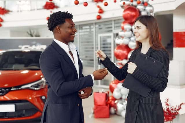 Woman handing keys to man at a car dealership