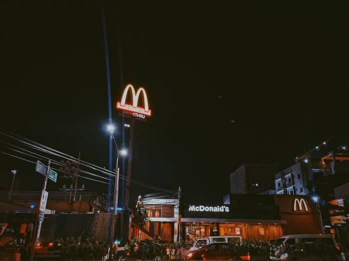 Night time, showing a Mcdonald's restaurant and sign, with cars in front of it, set in a city
