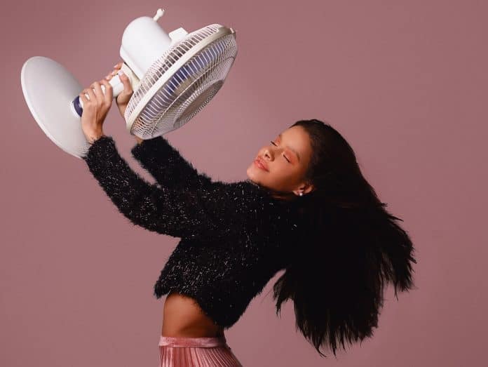 Woman in sparkly outfit, holding a fan up so it's blowing in her face