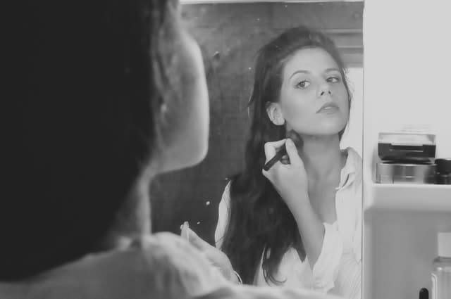 Woman putting on makeup in mirror