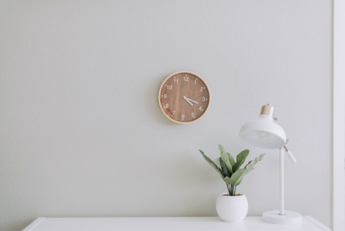 White desk with lamp against white wall, bamboo clock on wall