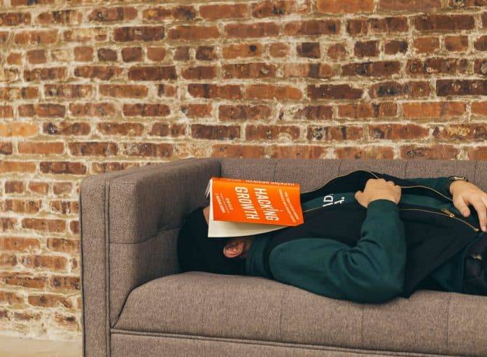 Person laying on a couch sleeping, with a book covering their face